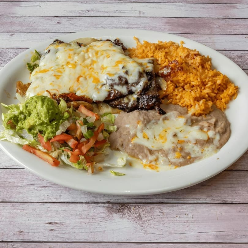 Cheesy steak with rice, refried beans, guacamole, and a side salad on a white plate.