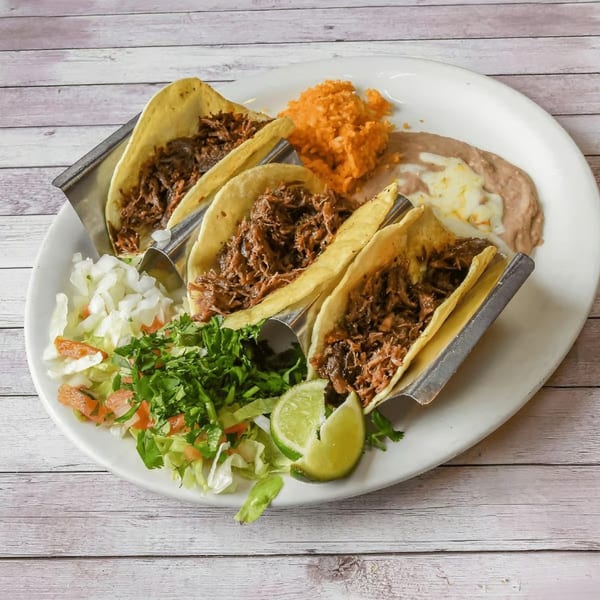 Three shredded beef tacos with rice, refried beans, and a side salad with lime wedges.