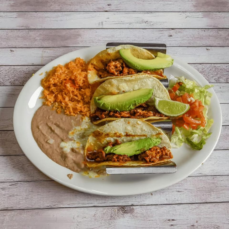 Three tacos with meat and avocado, served with rice, refried beans, and a side salad.