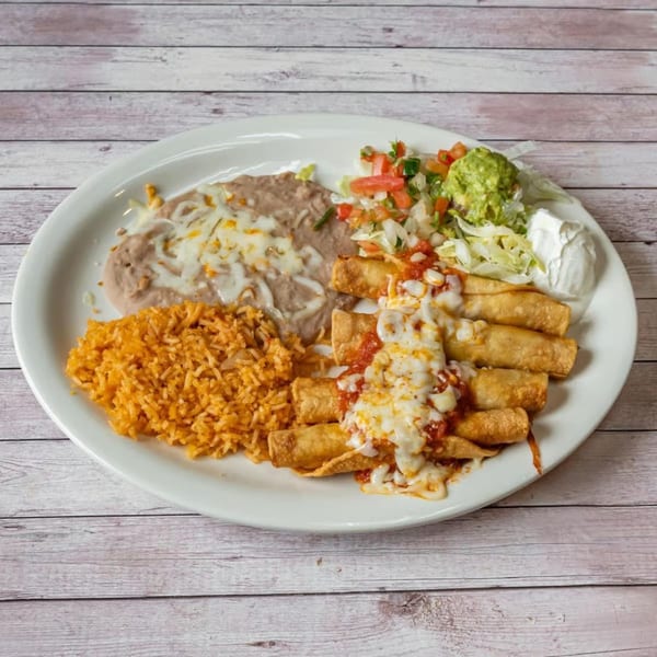 A white plate holds taquitos, rice, refried beans with cheese, and a side salad with guacamole and sour cream.